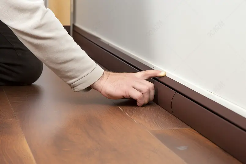 穿长袖的工人用手指食指按压在墙底的木质踢脚线