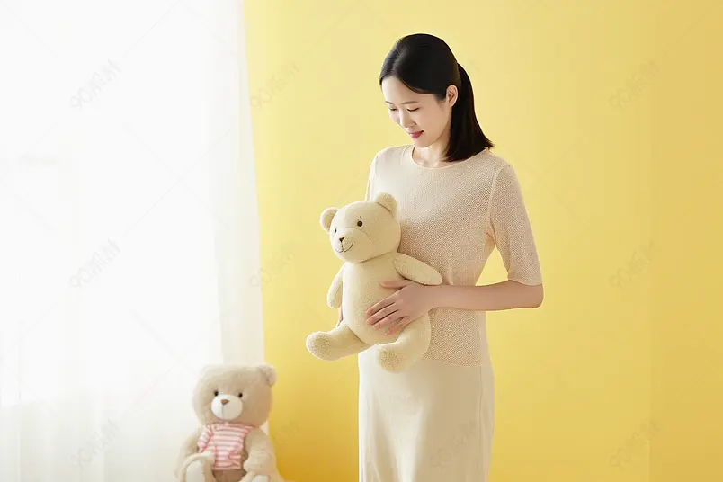 黄色墙壁怀孕的女性手抱着毛绒玩具
